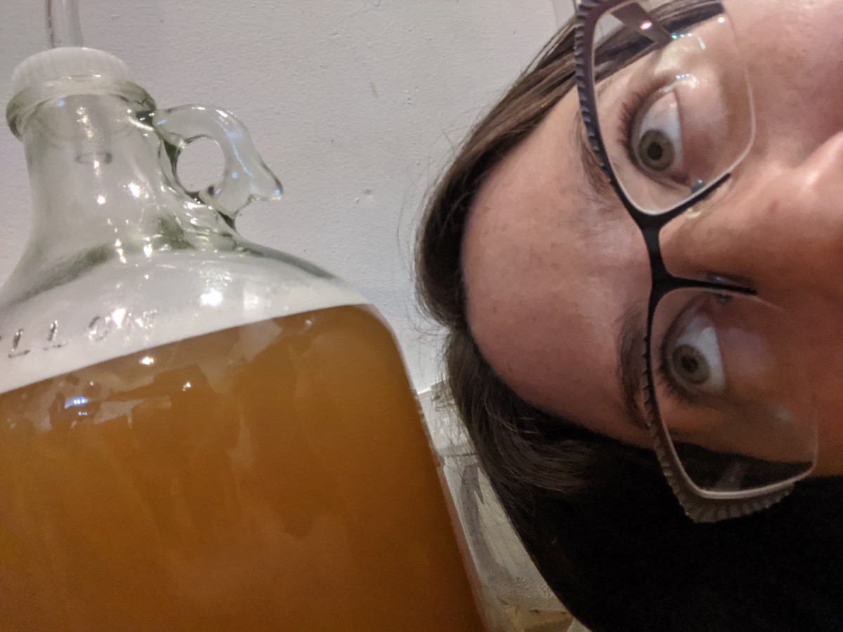 A jug of beer fermenting to the left, Jenna peeking into frame from the right